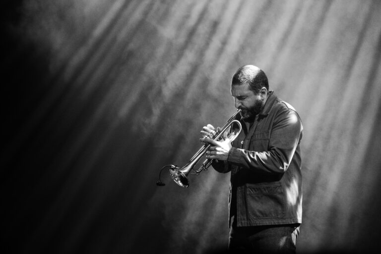 Een muzikant speelt op een trompet, omhuld door een sfeer van lichte stralen in zwart-wit.