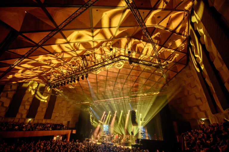 Een live concert met dramatische verlichting en een volle zaal in een moderne zaal.