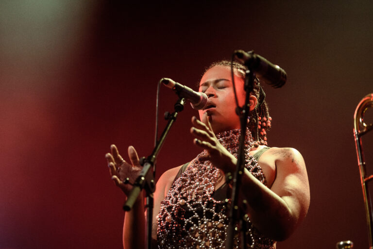 Zangeres met een glinsterende top, die emotioneel zingt in een live muzieksetting met microfoon.