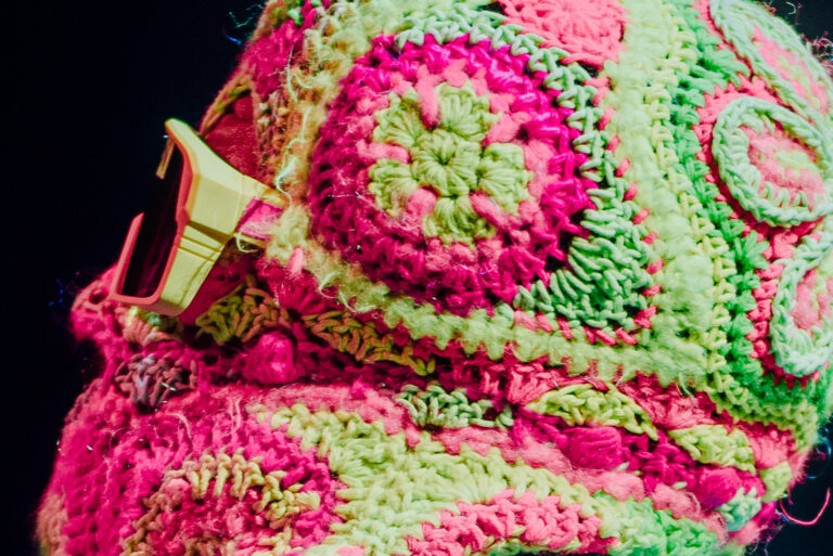 Een close-up van een kleurrijke, handgehaakte muts met roze en groene patronen.