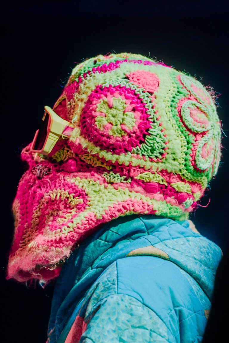 Een kleurrijke gehaakte muts met een opvallend ontwerp in heldere tinten van roze en groen, gedragen door een persoon.