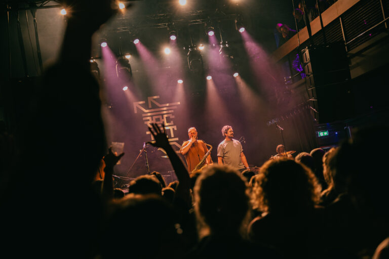 Een levendig live optreden op een podium met een enthousiast publiek en kleurrijke verlichting.