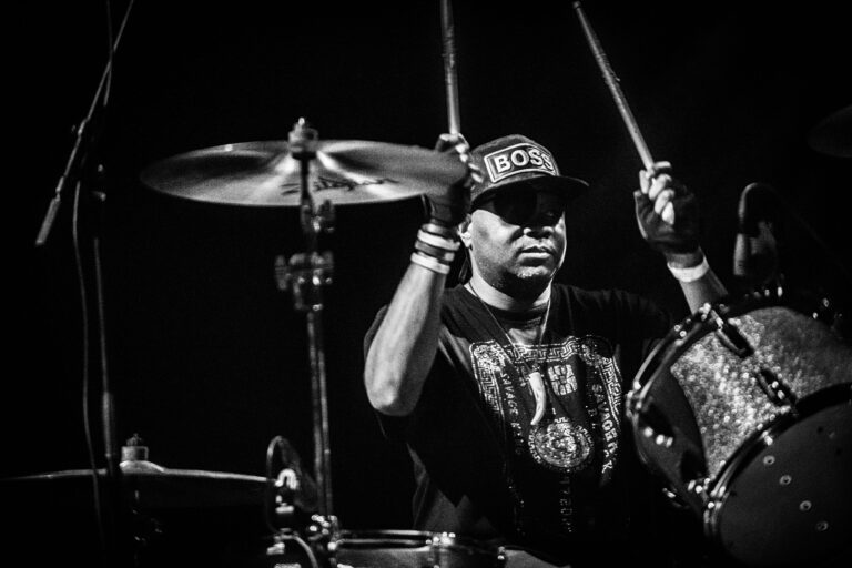 Een drummer speelt energiek op een drumstel in een zwart-wit afbeelding.