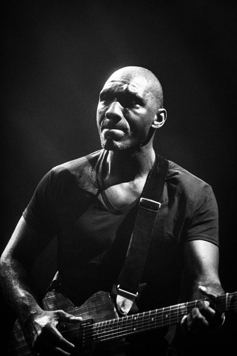 Een muzikant speelt op een elektrische gitaar tegen een donkere achtergrond.