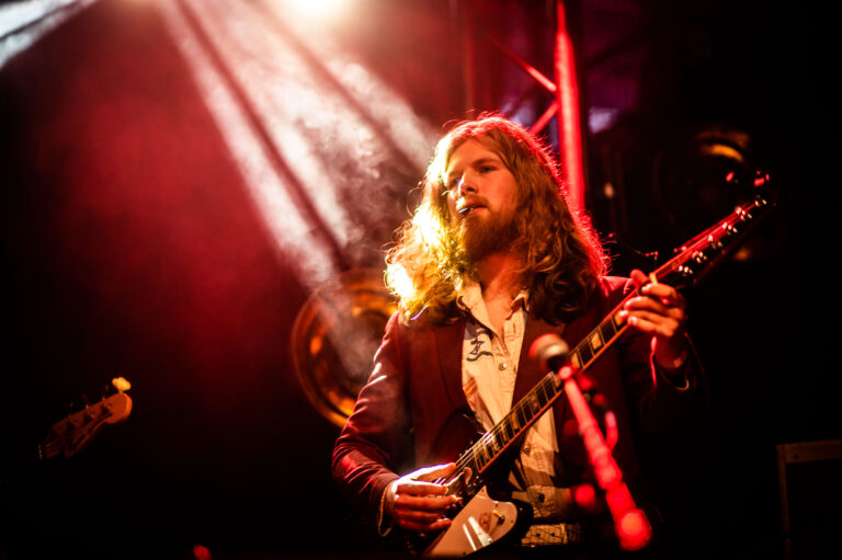 Een muzikant speelt op een elektrisch instrument onder kleurrijke lichten en lichteffecten.