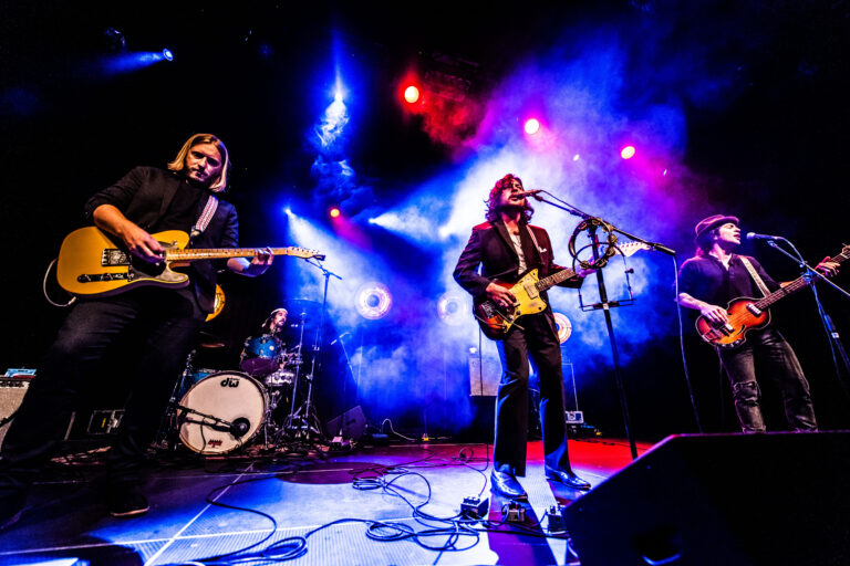 Een rockband treedt op met kleurrijke verlichting en instrumenten op een podium.