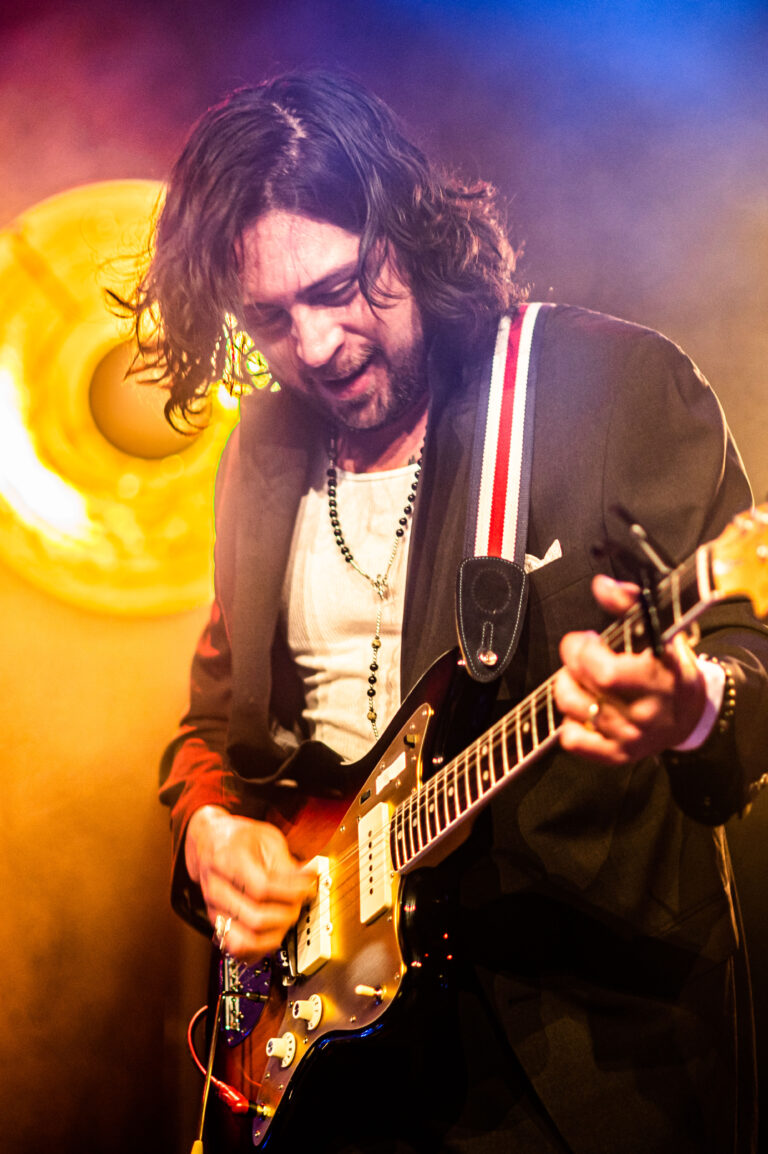 Een muzikant speelt gitaar op een podium met sfeervolle verlichting.