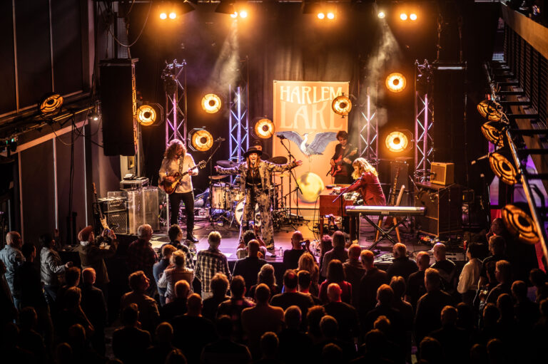 Een muzikale optreden met een band op een podium, verlicht door kleurrijke lichten, voor een enthousiast publiek.