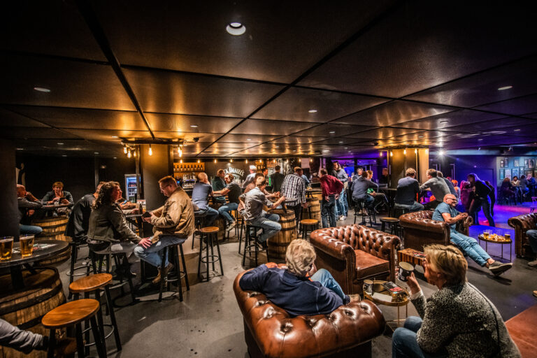 Een drukbezochte, sfeervolle bar met mensen die aan hoge tafels zitten en genieten van drankjes.