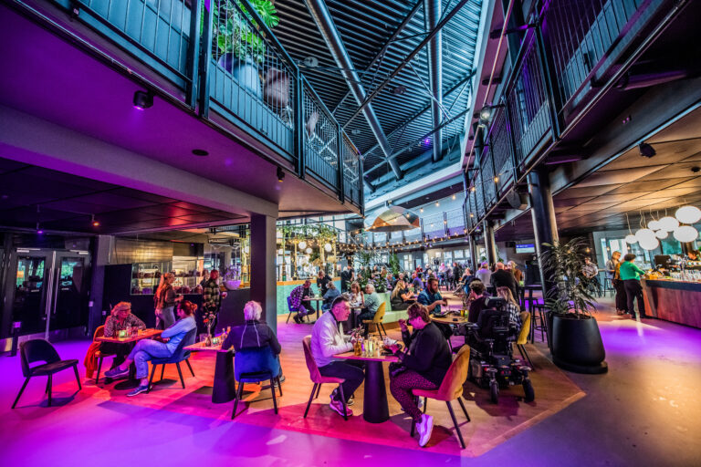 Modern café interior with colorful lighting and people enjoying drinks at tables.