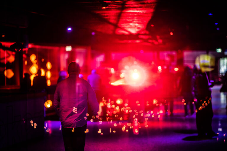 Een persoon wandelt door een kleurrijke, sfeervol verlichte ruimte met rode en paarse lichten.