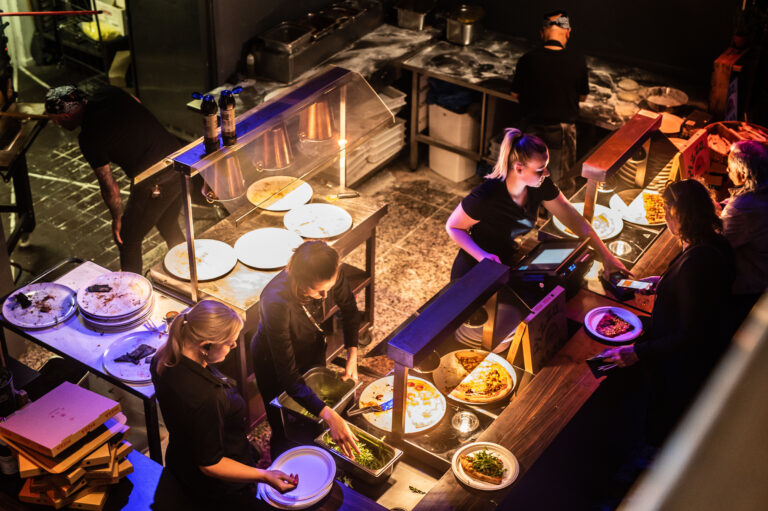 Een drukke keuken met medewerkers die maaltijden bereiden en serveren aan een buffet.