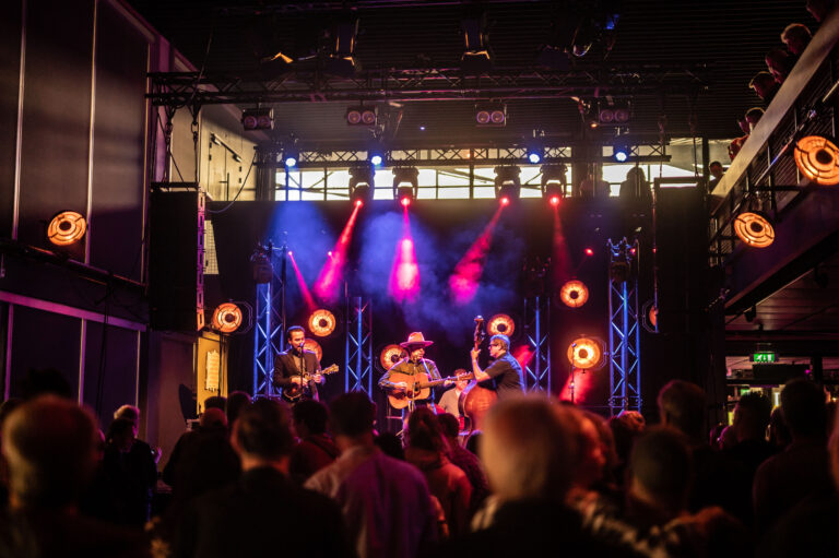 Een band speelt live op een podium met kleurrijke verlichting voor een publiek.