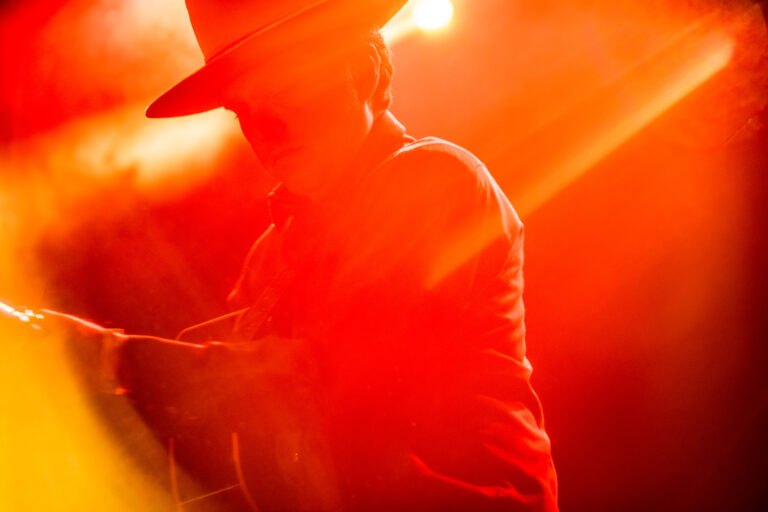 Silhouet van een persoon met een hoed tegen een achtergrond van vurige verlichting.