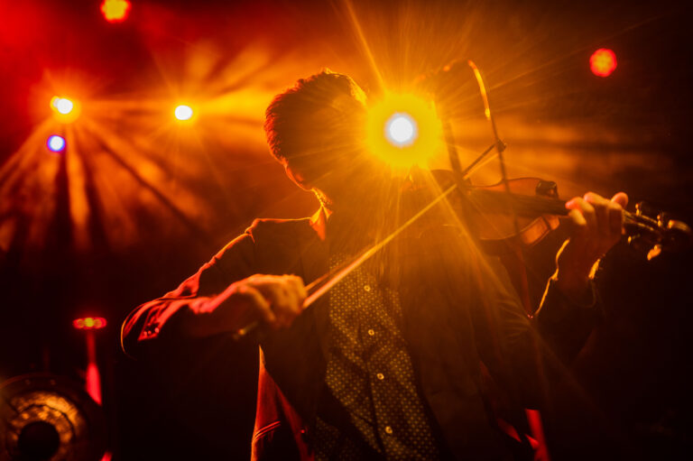 Een muzikant speelt viool op een podium met kleurrijke verlichting.
