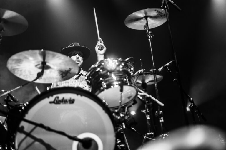 Een drummer speelt op een drumstel met een opvallende lichtinval in zwart-wit.