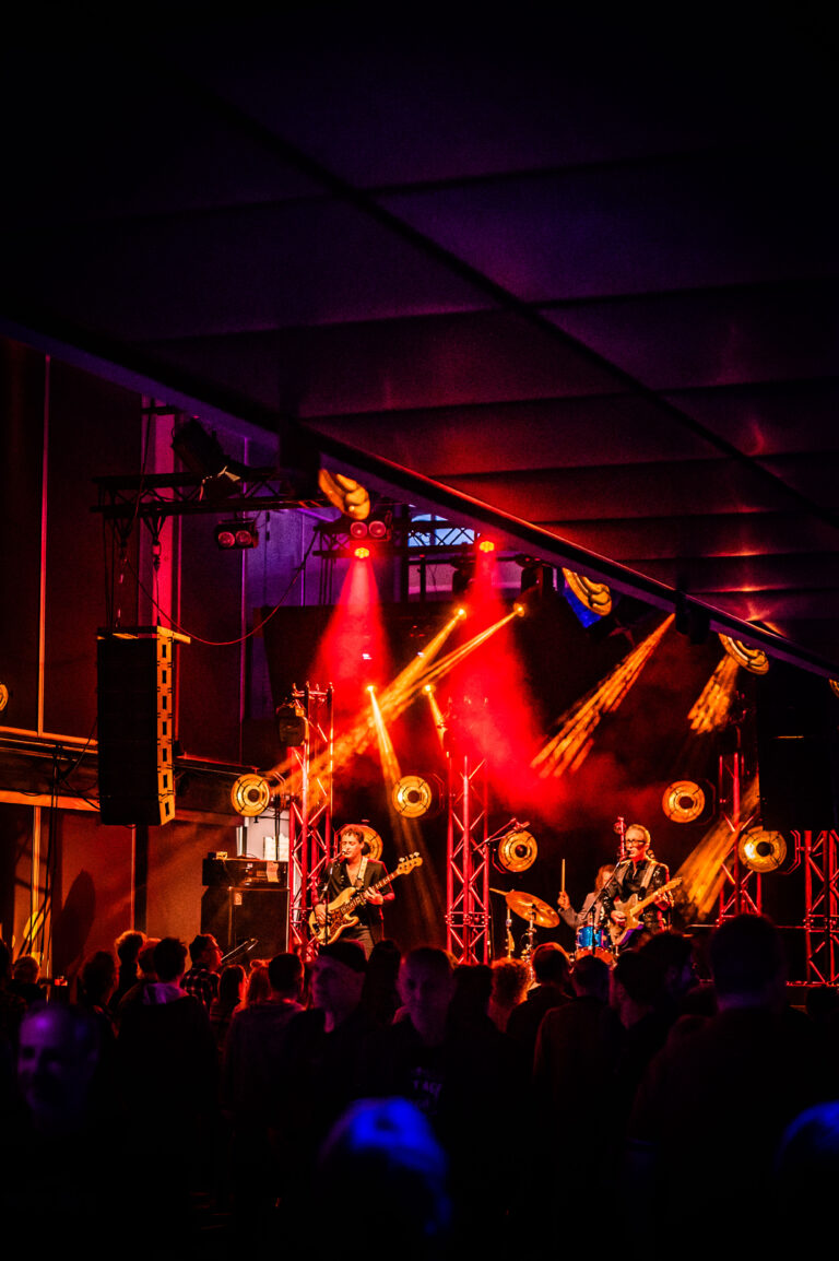 Een liveband speelt op een podium, omgeven door een menigte en kleurrijke verlichting.