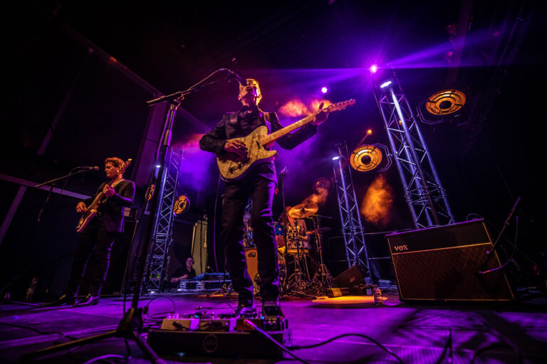 Een band speelt live op het podium met kleurrijke lichten en een energieke sfeer.