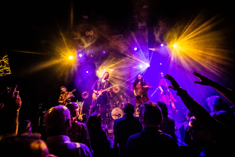 Een energiek live-optreden van een band met kleurrijke verlichting en een enthousiast publiek.