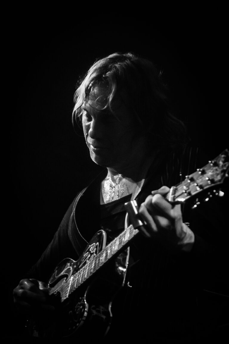 Een muzikant speelt op een gitaar tegen een donkere achtergrond.