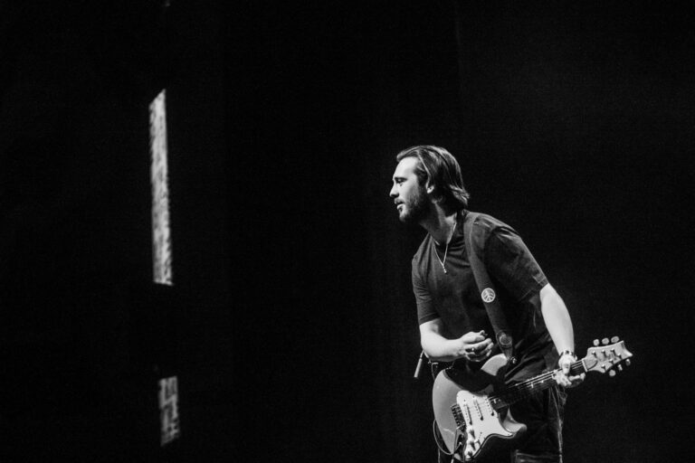 Een muzikant speelt gitaar op het podium in een zwart-wit afbeelding.