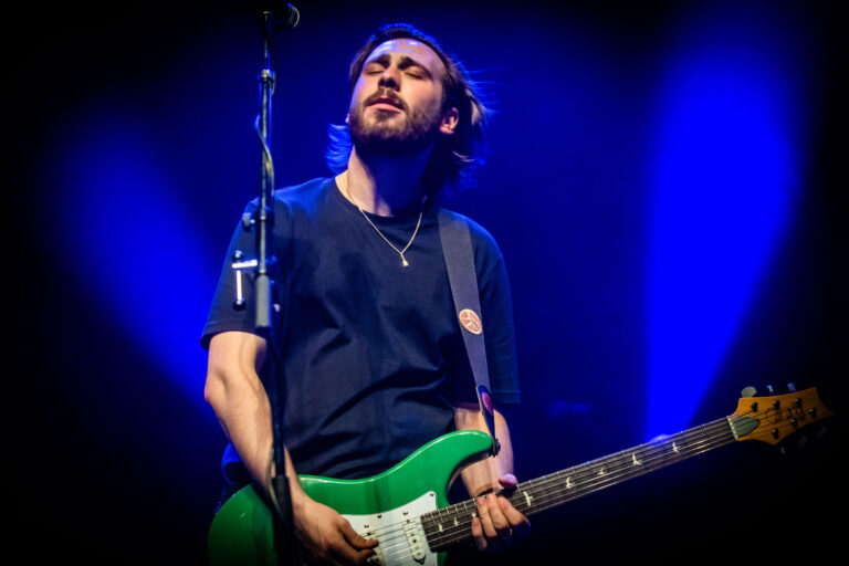 Een muzikant speelt op een groene gitaar tegen een achtergrond van blauwe lichten.