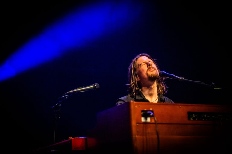 Een muzikant speelt een toetseninstrument op een podium met een blauwe belichting.