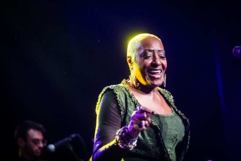 Een zangeres met een kort kapsel, gekleed in een groene outfit, die met een glimlach optreedt op het podium.