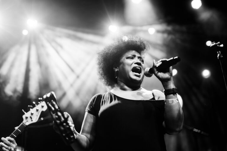 Een vrouw zingt krachtig in een live muzieksetting, omgeven door theatrale verlichting.