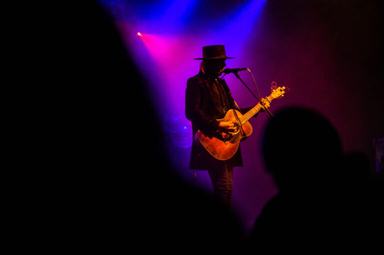 Een silhouet van een muzikant die een gitaar speelt op een podium met kleurrijke verlichting.