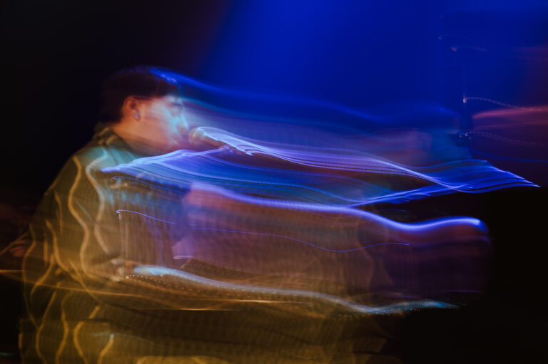 Een muzikant is te zien met een microphone, omgeven door dynamische kleurrijke lichteffecten.