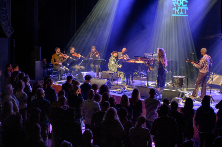 Een live muziekoptreden met een band op het podium en een enthousiast publiek in de zaal.