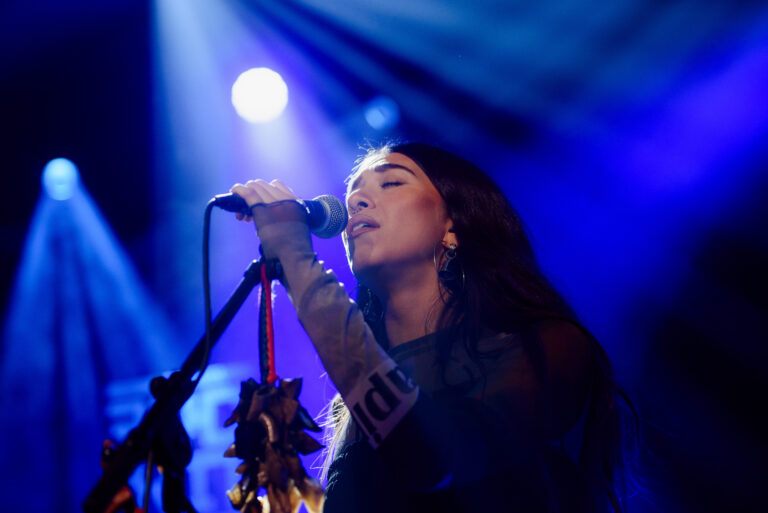 Zangeres die emotioneel zingt met een microfoon onder een blauwe en paarse lichteffect.