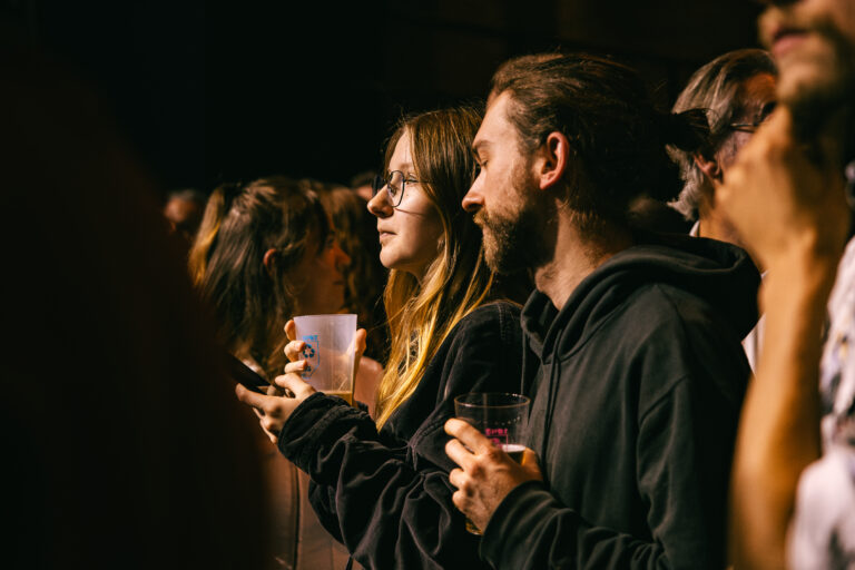 Een groep mensen staat dicht bij elkaar, met glazen in de hand, terwijl ze naar een evenement kijken.