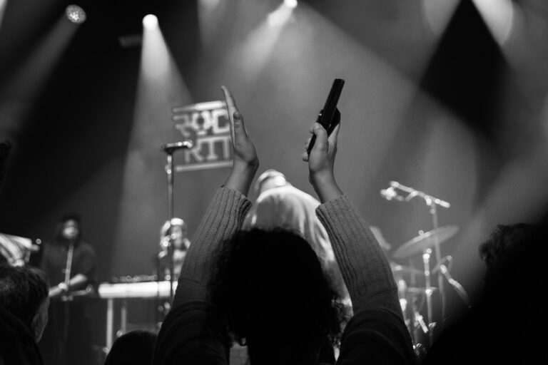 Een publiek met opgestoken handen geniet van een liveoptreden, verlicht door schijnwerpers.