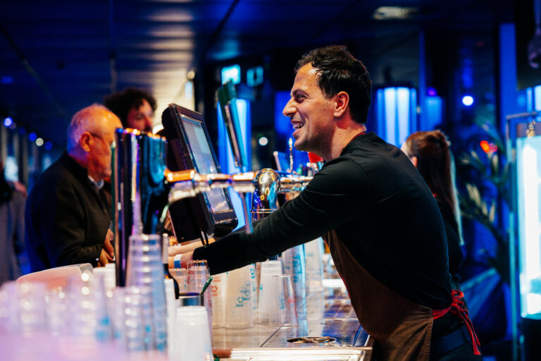 Een barman schenkt drank in aan een drukke bar met blauwe verlichting.