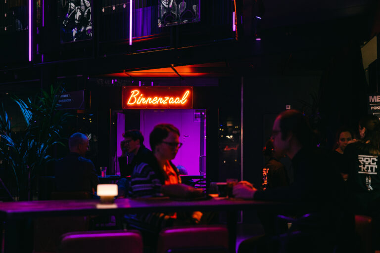 Een sfeervolle bar met neonverlichting en mensen die ontspannen aan tafel zitten.