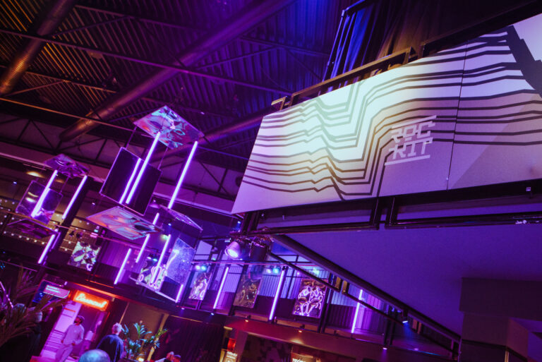 Een modern interieur met kleurrijke verlichting en kunstwerken, waaronder een groot geprojecteerd logo op een muur.