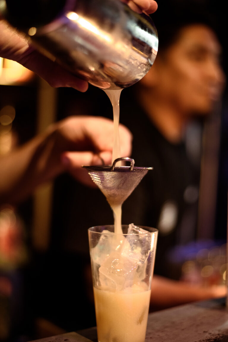 Een barman giet een gemixt drankje door een zeef in een glas met ijs.