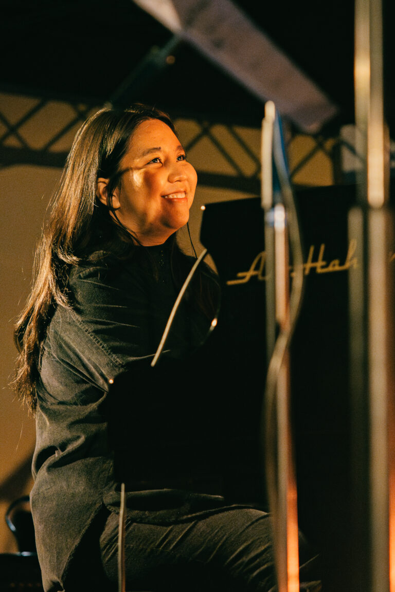 Een muzikante die zittend aan een piano glimlacht tijdens een optreden.