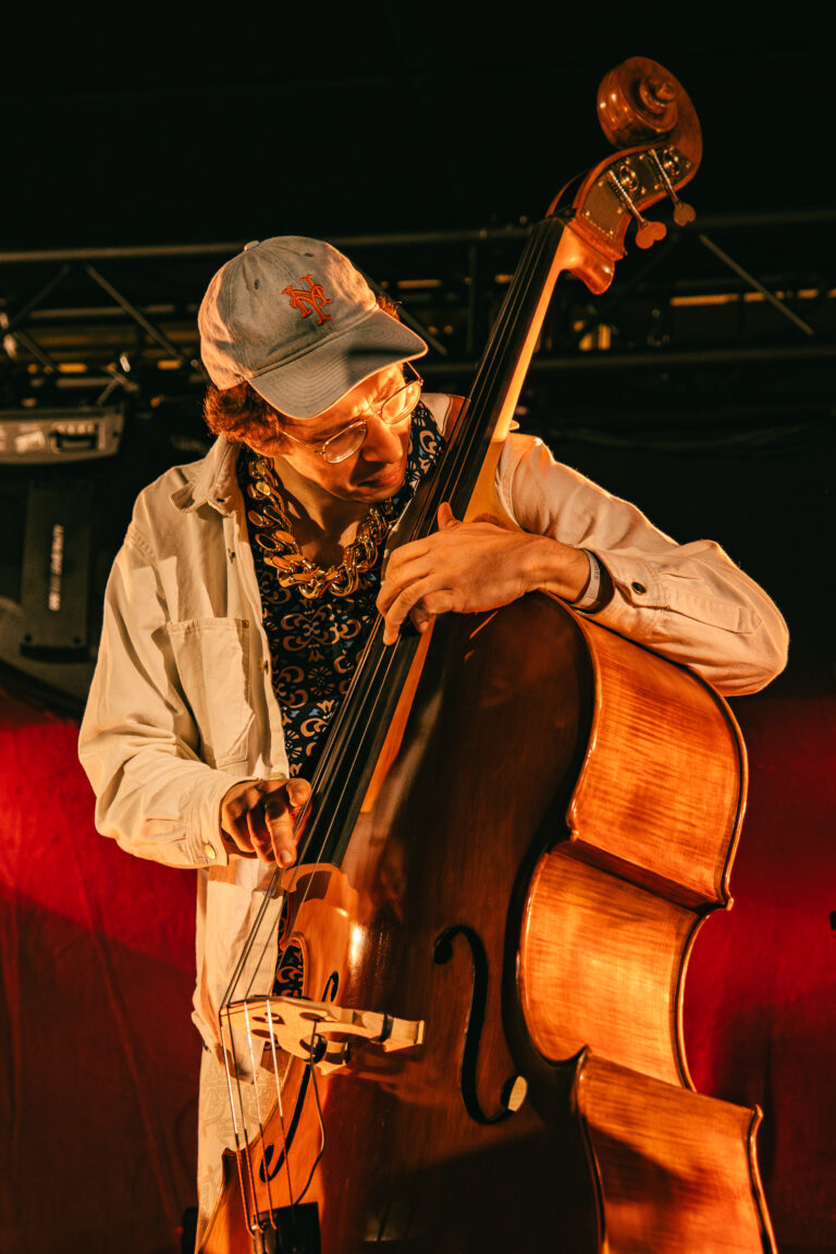 Een muzikant speelt op een contrabas tijdens een optreden, met een kleurrijke achtergrond.