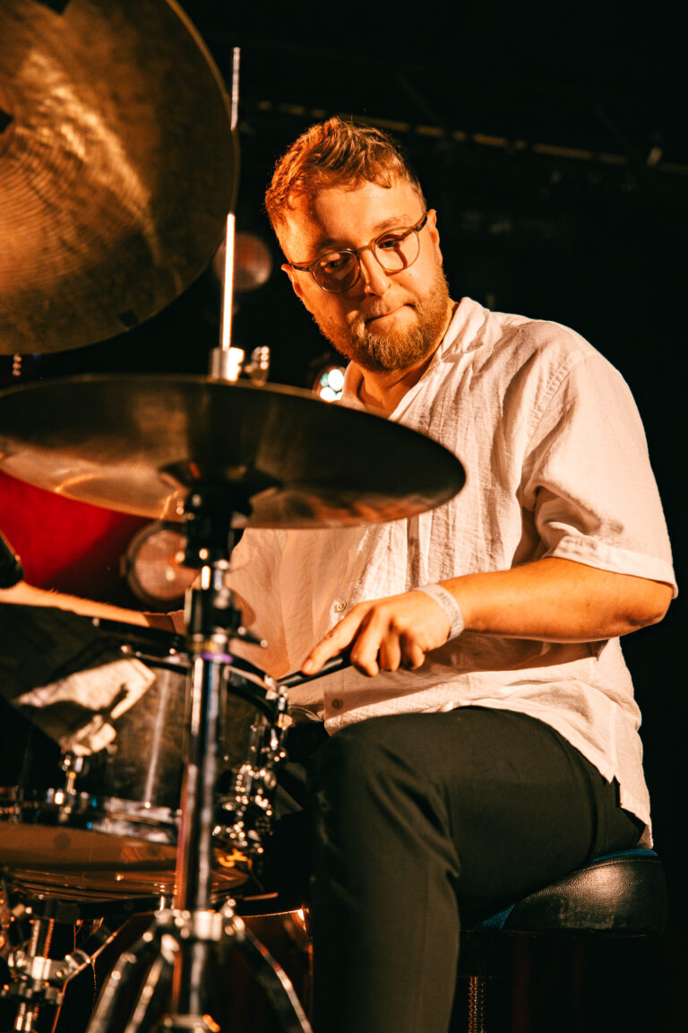 Een man speelt op een drumstel tijdens een live muziekoptreden.