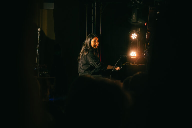 Een artiest speelt muziek op een podium, verlicht door enkele spots.