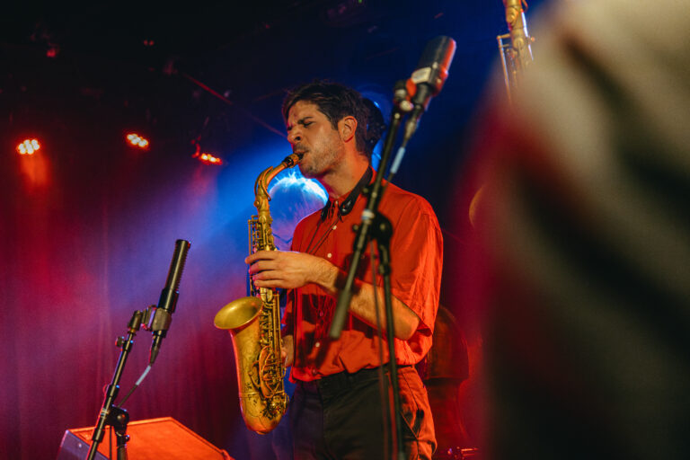 Een muzikant speelt saxophone op een podium met kleurrijke verlichting.