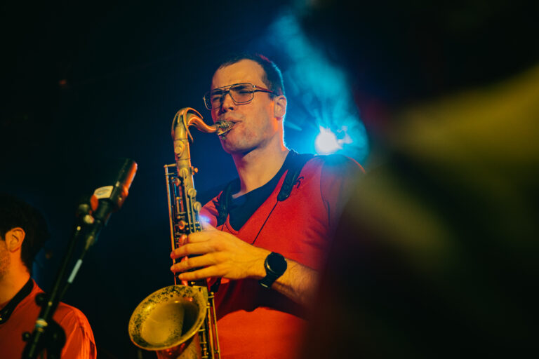 Een muzikant speelt saxofoon op een podium met blauwe verlichting.