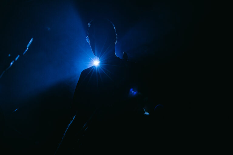 Silhouet van een persoon tegen een blauwe gloed en donkere achtergrond.