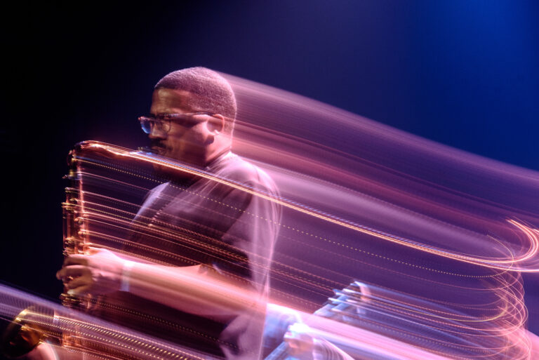 Een muzikant met een saxofoon staat op het podium, omgeven door dynamische lichtstrepen.