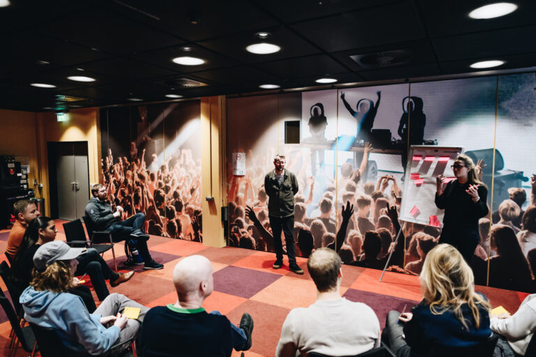 Een groep mensen zit in een zaal terwijl twee sprekers een presentatie geven voor een achtergrond met een publiek.