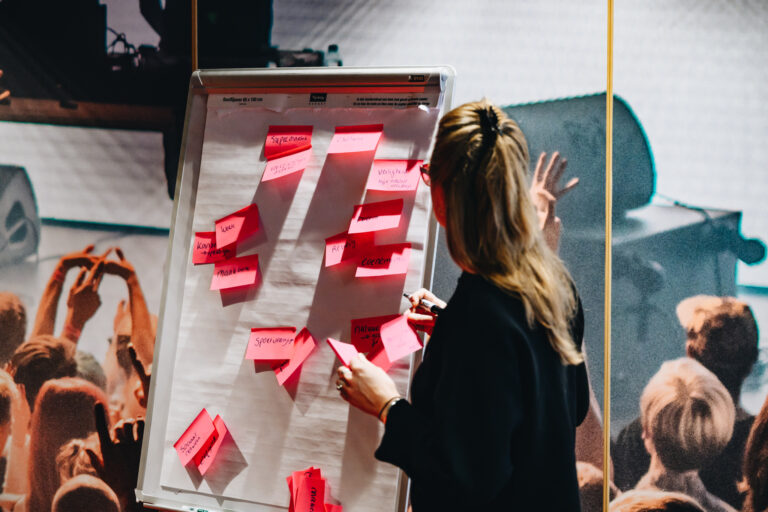 Een persoon plakt roze post-its op een flip-over tijdens een brainstormsessie.