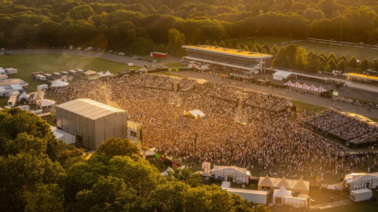 Een uitgestrekt publiek verzameld voor een muziekfestival in een groene omgeving tijdens zonsondergang.